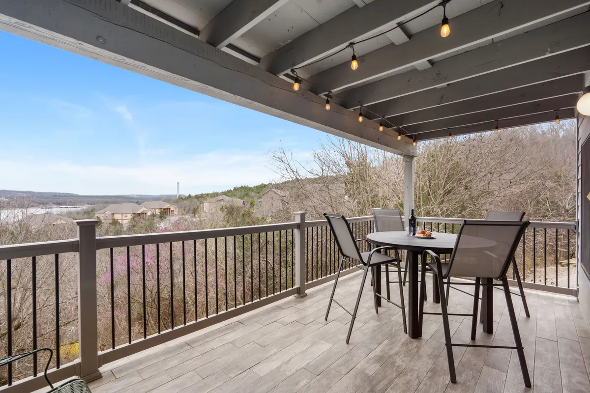 An outdoor seating area with tables and chairs is set against a scenic landscape and illuminated by charming string lights overhead. The tranquil setting suggests pleasant evenings and social gatherings, extending the poolside experience into relaxed outdoor dining or winding down after a swim.
