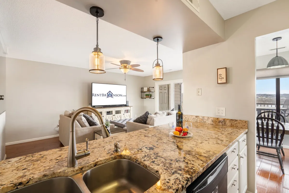 A seamless view of the living area merging into the kitchen, showcasing a granite countertop, a plush sofa, and a television unit. The layout demonstrates the open flow between relaxing spaces and the kitchen, with plenty of natural light creating an airy, connected feel.