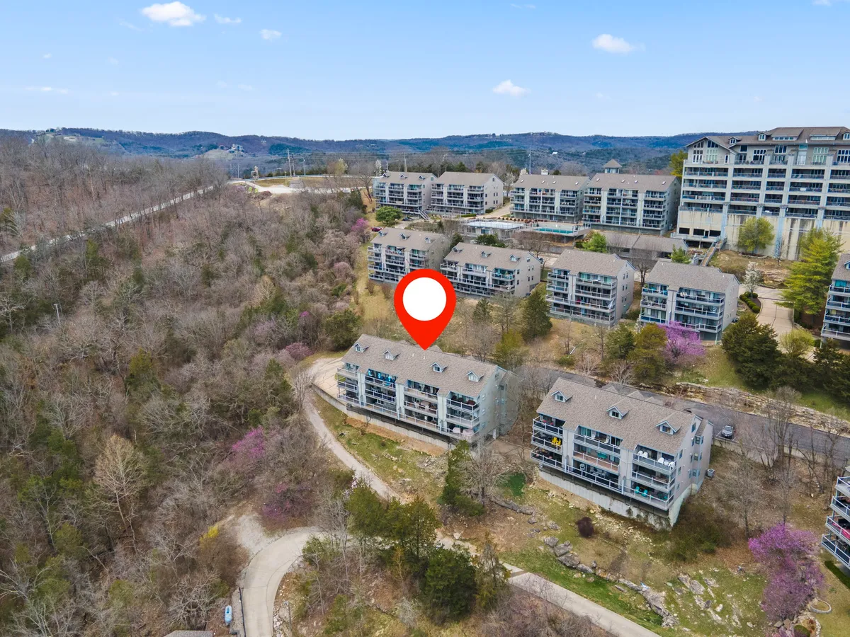 Rows of multi-story condominiums are nestled amid greenery, with a winding road inviting exploration of the neighborhood. The tranquil setting is perfect for nature walks and community events, with views of the surrounding hills.