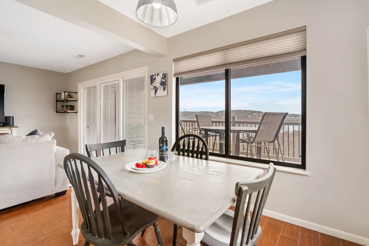 A dining table set beside a window, offering glimpses of the lake outside. On the table are a bottle of wine and a plate of fruit, inviting guests to share meals and enjoy each other's company while taking in the views.