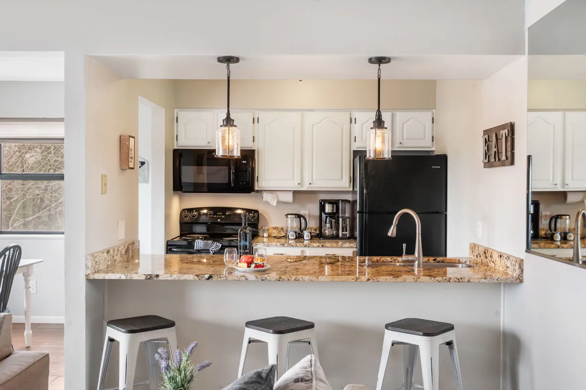 This image showcases a stylish kitchen with granite countertops, modern black appliances, and pendant lights hanging above a spacious bar with comfortable stools. The setup is perfect for both cooking and socializing, with an open layout that invites conversation and shared activities.