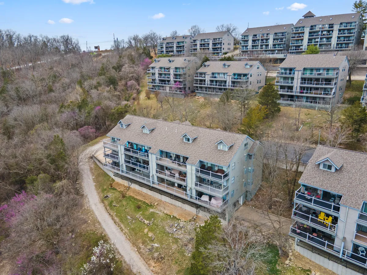 Multiple apartment buildings nestled in green surroundings, with balconies adorned with personal touches and quiet paths weaving through the area. The natural landscaping, combined with visible outdoor living spaces, highlights both privacy and community amenities.