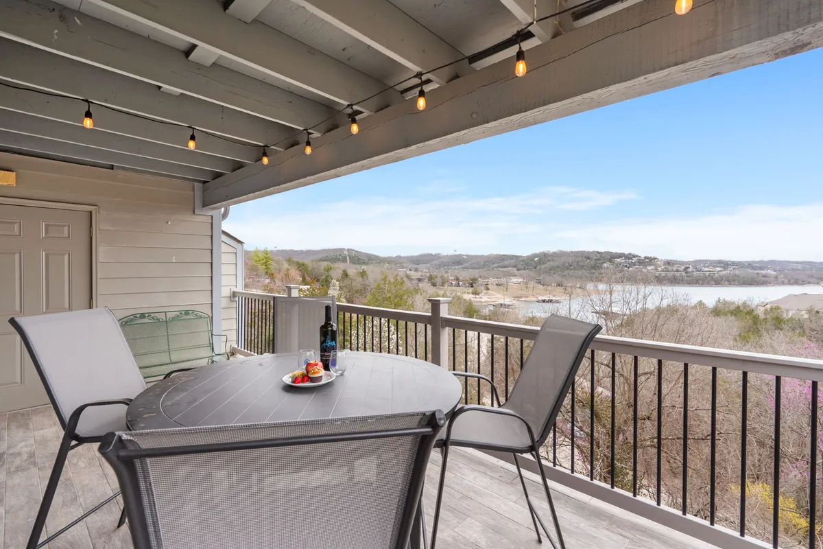 An outdoor table is elegantly set with wine, snacks, and glasses, all under a string of glowing lights. In the background, there's a scenic landscape view, suggesting a welcoming spot for gathering and enjoying the outdoors.