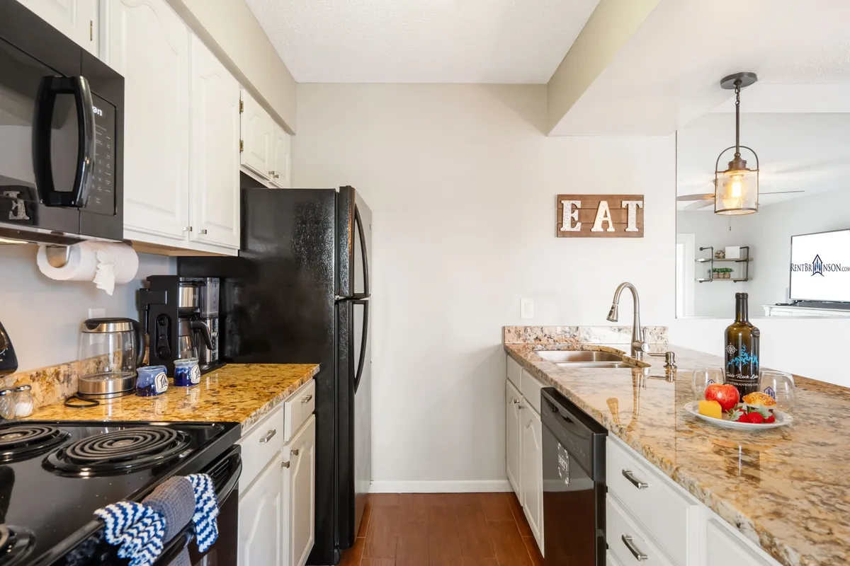 A bright, inviting kitchen with granite countertops, modern black appliances, a decorative sign, and a bowl of fresh fruit. The space is ready for meal prep and socializing, perfect for families preparing picnics or gathering after a day at the park.