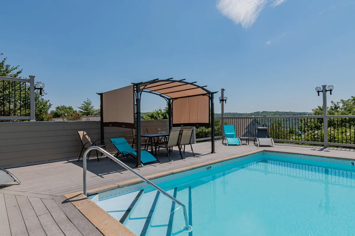 A bright, inviting outdoor swimming pool is surrounded by lounge chairs and a covered gazebo seating area. The landscape view in the background provides a tranquil resort feel, perfect for sunny days of relaxation and family fun. The setup encourages both group gatherings and personal downtime by the water.